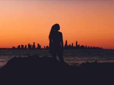 Frau steht vor einer Skyline während des Sonnenuntergangs