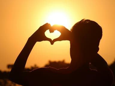 Person zeigt Herz vor Sonne