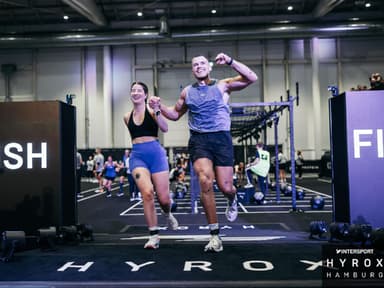 Redakteurin Laura hat mit ihrem Freund einen Hyrox-Wettkampf mitgemacht. Eine Frau und ein Mann laufen Hand in Hand in Sportkleidung auf die Kamera zu.