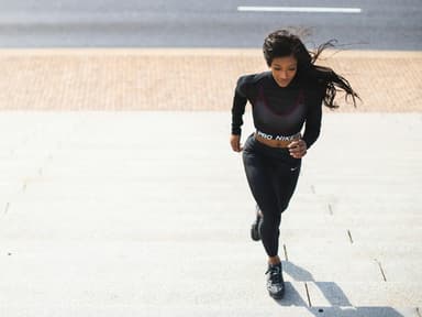 Laufen ist 2026 nach wie vor ein großes Thema. Frau in schwarzem Sport-Outfit läuft draußen Treppenstufen hoch.