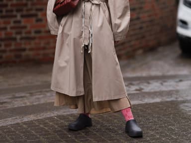 Frau im beigen Mantel mit Garden Shoes und einer weinroten Tasche.