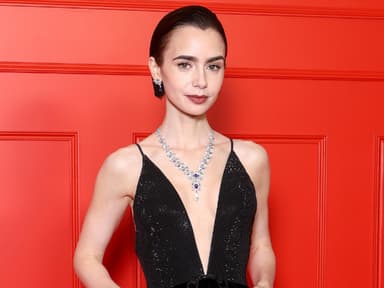 Lily Collins in einem schwarzen Abendkleid mit tiefem V-Ausschnitt vor einer roten Wand.