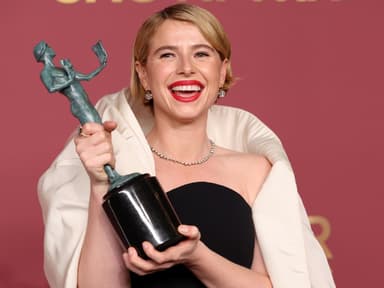 Jessie Buckley mit einem Award in der Hand strahlt in die Kamera.