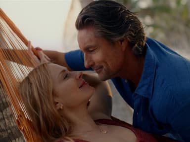 Eine Frau auf einer Hängematte lächelt einen Mann an, der über sie gebeugt ist.