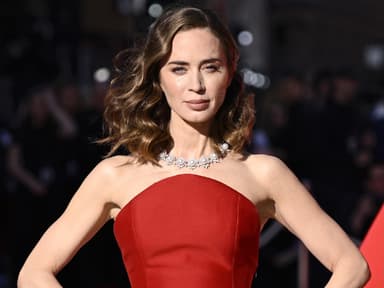 Emily Blunt mit einem roten Kleid stemmt die Hände in die Hüfte.