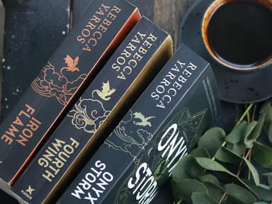 Drei Bücher liegen hochkant auf einem Tisch mit einer Tasse Kaffee und Eukalyptus-Sträuchern.