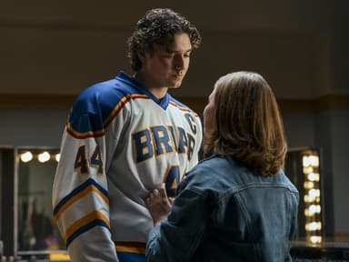 Ein junger Mann im Eishockey-Trikot steht einer jungen Frau in Jeansjacke gegenüber und guckt zu ihr herunter.