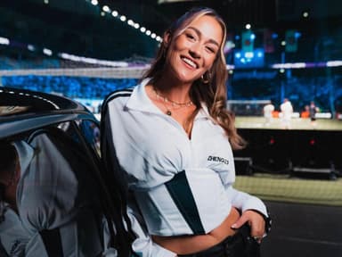 Eleni Frommann begleitet sechs Wochen lang die Fußball-Weltmeisterschaft in den USA. Eine junge Frau in einem weißen Sportoberteil lehnt gegen ein Auto und lacht in die Kamera.