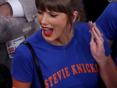Taylor Swift sorgte mit ihrem Graphic Shirt beim Knicks Spiel für Aufsehen. Taylor Swift mit einem blauen Shirt schreit euphorisch und schaut zur Seite nach links.