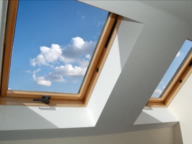 Im Sommer kann eine Dachgeschosswohnung zum Verhängnis werden. Dachgeschoss Fenster aus Holz mit Blick auf den blauen Himmel mit Wolken.